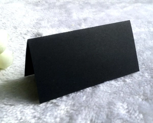 Close-up of black pearlescent folded name card with a matte texture on white plush surface