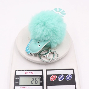 Detail shot showing a light green seahorse pompom keychain weighing 26g on a digital scale