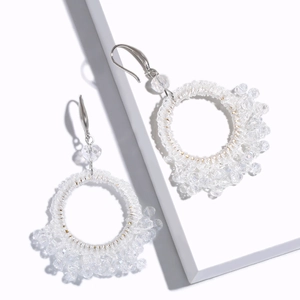 Detail of white beaded hoop earrings with intricate handmade woven patterns and metal hooks