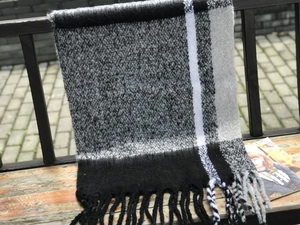 Detail of thick black and white plaid scarf with soft tassels on a wooden bench