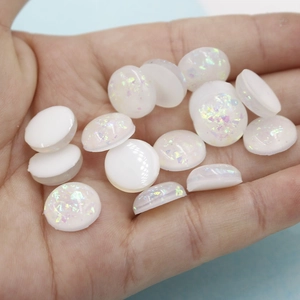 Macro shot of 12mm white oval resin cabochons with iridescent foil flakes on a hand palm