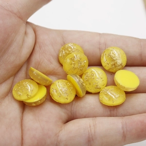 Detail of 12mm yellow synthetic opal resin cabochons with gold foil flakes in palm