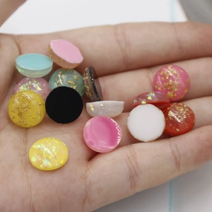 Close-up of colorful 12mm synthetic opal resin cabochons with gold foil flakes in a hand