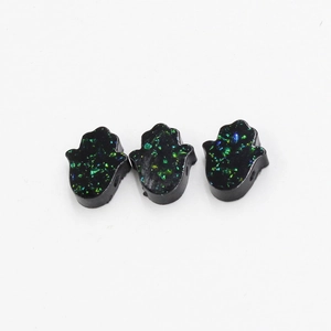 Detailed view of three black resin Hamsa hand beads with blue and green glitter