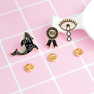 Vue détaillée de l'ensemble de broches émaillées baleine, médaille et oeil sur fond rose