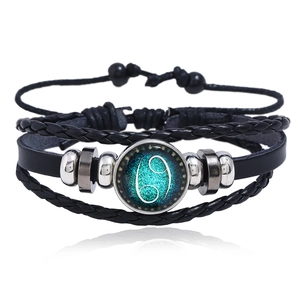 Detail of multi-layer black leather bracelet with glowing Cancer zodiac glass charm