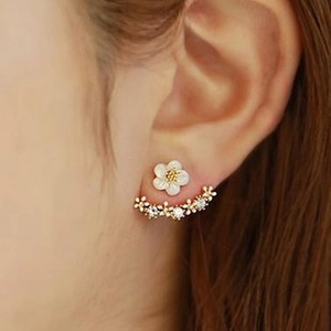 Close-up of asymmetrical golden earring set featuring white flowers and crystal fringe