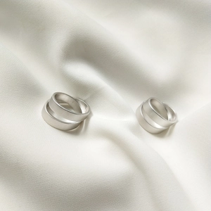 Close-up of dual-layer matte S925 sterling silver rings on white pleated silk fabric