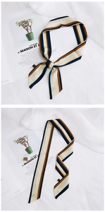 Detail of a beige silk scarf with navy and brown stripes tied in a bow on a magazine
