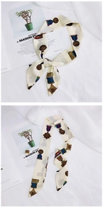 Detail of a beige silk scarf with colorful medal patterns tied in a bow over a magazine