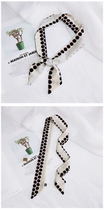 Detail of long beige silk scarf with black and red polka dots tied in a bow on a magazine