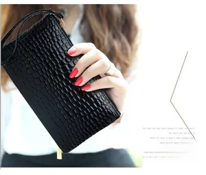 Detail of black crocodile embossed clutch featuring golden zipper and wrist strap
