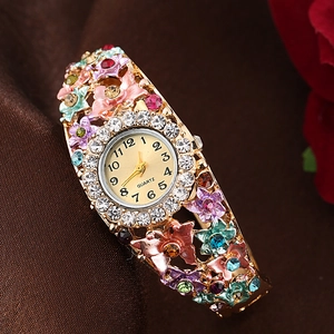 Detailed close-up of a gold floral bangle watch with colorful crystals and enamel flowers