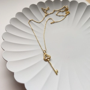 Macro shot of a minimalist gold key pendant necklace on a textured display tray