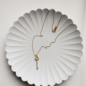 Macro shot of gold clover key pendant necklace on elegant white pleated texture plate