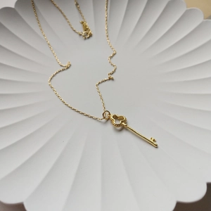 Top view of a gold key pendant necklace with heart details on a white petal ceramic plate