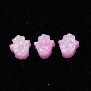 Macro view of three pink opal Hamsa hand charms for jewelry making on black velvet