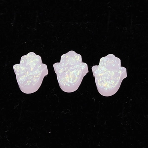 Macro detail of three pink synthetic opal hamsa charms with iridescent finish on velvet