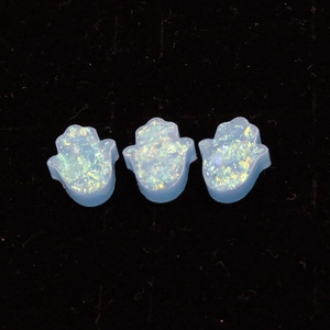 Macro shot of three blue synthetic opal Hamsa hand charms on black velvet background