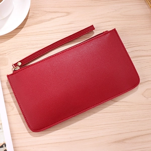 Red pebbled leather wallet clutch with gold zipper and wrist strap on wooden table