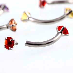 Macro shot of curved eyebrow piercing showing screw thread and colorful zircon stones