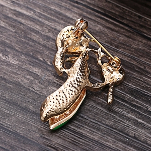 Back view of gold pea pod brooch with pearl and green stone on dark wood background