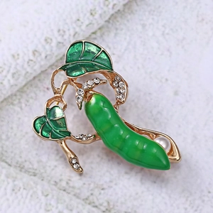 Macro detail of pea pod brooch with green enamel, gold plating and white pearls
