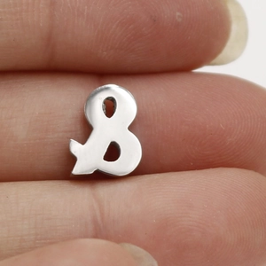 Close-up of a silver polished stainless steel ampersand charm held between fingers