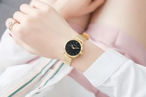 Detail of elegant gold mesh band watch with black dial and clover ring accessory