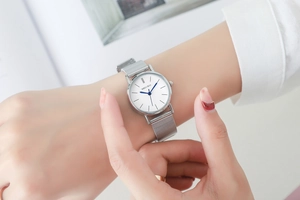 Close-up of a silver mesh strap watch with blue hands on a wrist for daily wear