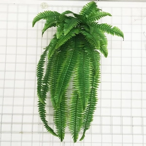 Close-up of artificial hanging fern vine with lush green plastic leaves on a wall grid