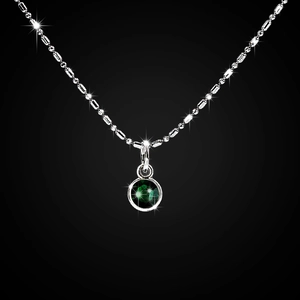 Macro view of silver necklace with green gemstone pendant on dark background
