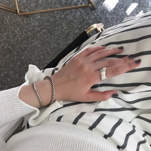 Close-up of minimalist silver criss-cross ring and layered twisted rope chain bracelets