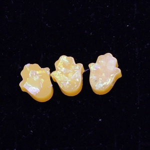 Macro shot of three translucent orange resin Hamsa Hand pendants with glitter flakes