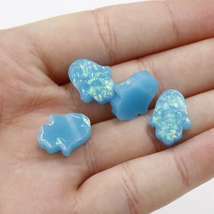 Close-up of four blue resin Hamsa hand pendant beads held in a hand for scale