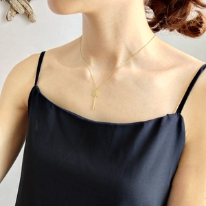 Close-up of a gold clover key pendant necklace worn by a model in a natural setting