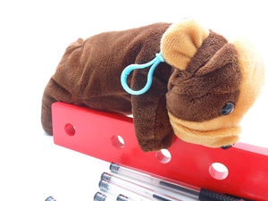 Close-up of brown plush puppy pencil case with blue clip and stationery on white background