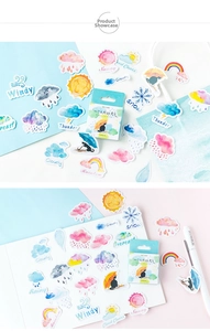 Macro detail of watercolor weather stickers showing sun, rainbow and clouds on a notebook