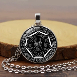 Macro detail of silver necklace featuring a black scorpion glass dome pendant on wood