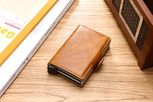 Brown dual-layer leather wallet with push-button pop-up mechanism on a wooden desk