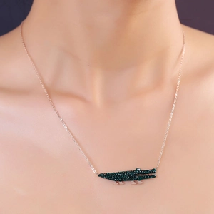 Gros plan d'un collier en or rose avec pendentif crocodile en cristal vert sur le cou