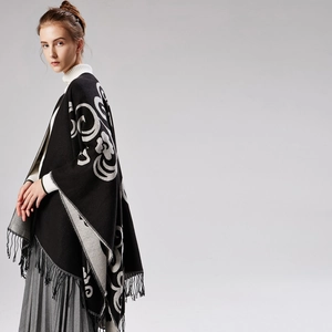 Knitted black shawl with grey patterns and fringe trim worn over a white turtleneck