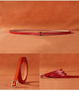 Close-up of slim red leather belt with gold metal buckle and smooth textured finish