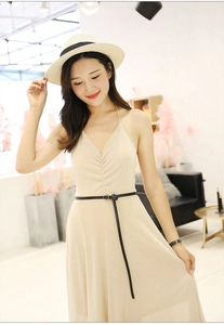 Detail of a slim black leather belt styled on a beige summer maxi dress with a straw hat