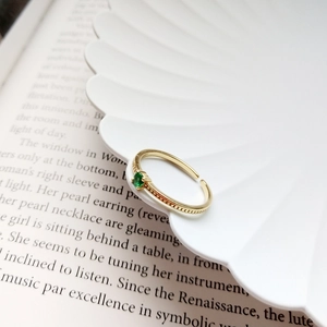 Close-up of a vintage adjustable gold ring with a green gemstone and beaded texture