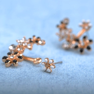 Detail of light gold floral earrings with black and white enamel petals and rhinestones