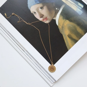 Detailed shot of golden round pendant necklace on Girl with a Pearl Earring book