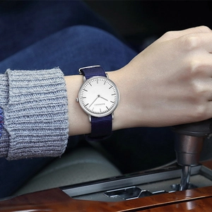 Blue nylon strap watch with white dial and silver case worn on hand in a car interior