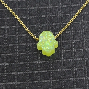 Macro shot of gold Hamsa hand pendant necklace with green synthetic opal inlay detail