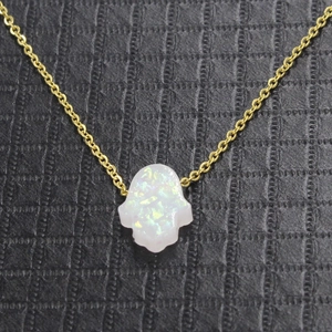Close-up of golden Hamsa hand pendant with iridescent white opal on black leather